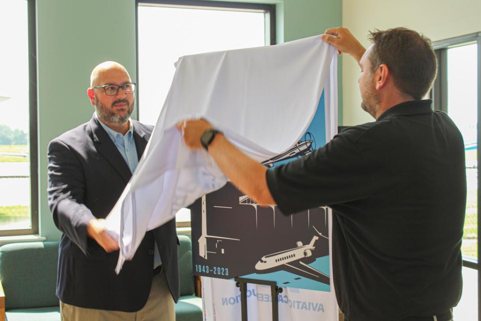 Micah Risher and Jeff Lankford unveil the official artwork for the 80th Anniversary. Created by Bay Imprint, the artwork honors the airport with a homage to the past and images of the future.